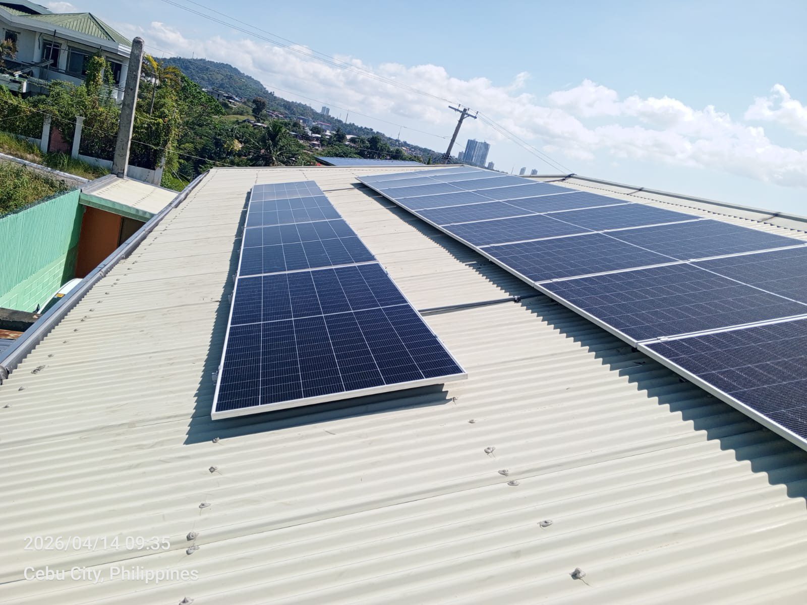 Two large solar sub-arrays spanning a white corrugated rooftop in Cebu City, with the city skyline and an open horizon behind — a wider commercial-scale install.