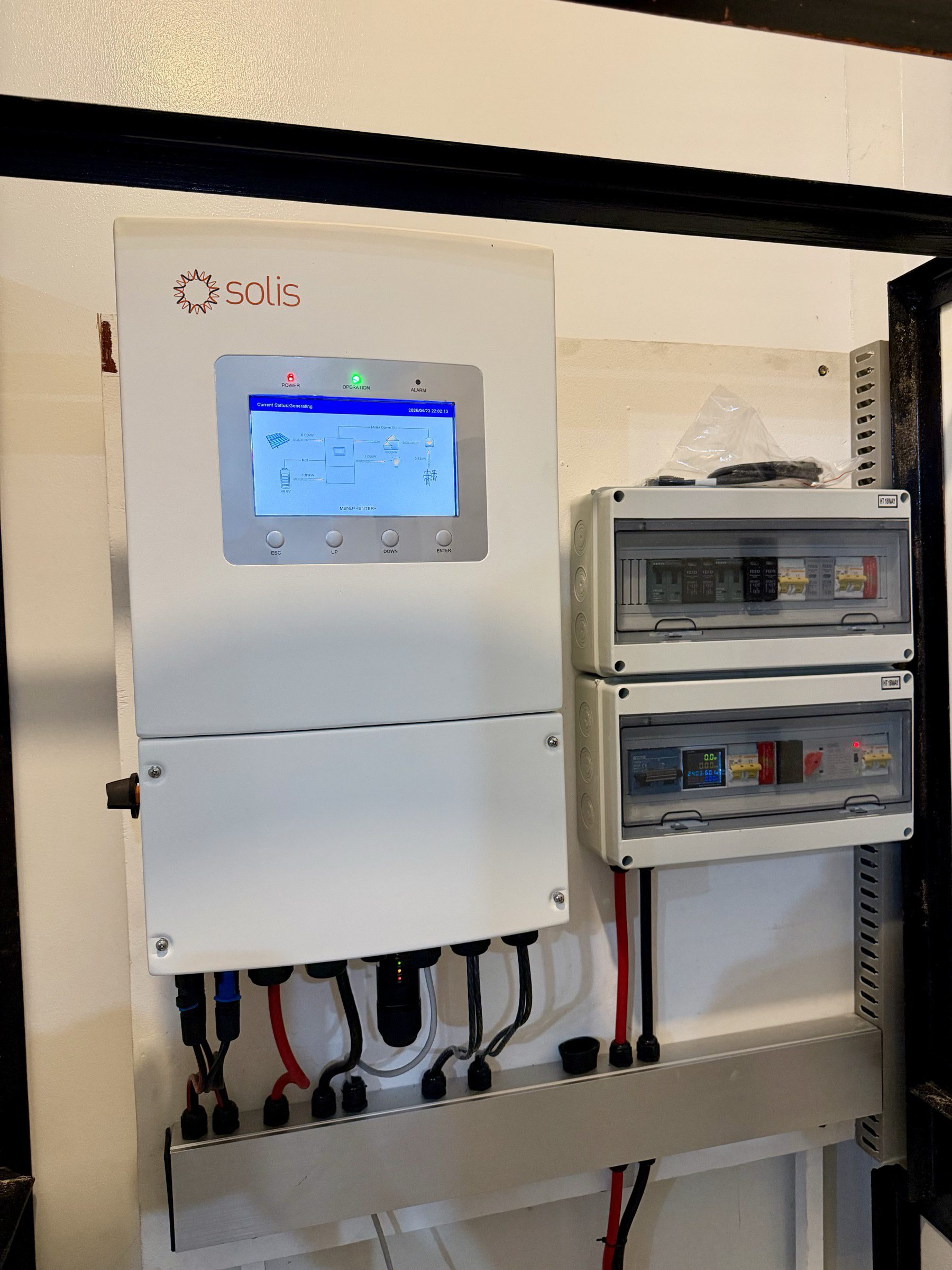 The finished Solis hybrid inverter mounted inside its cabinet on commissioning day, screen reading 'Current Status: Generating', combiner boxes neatly attached either side.